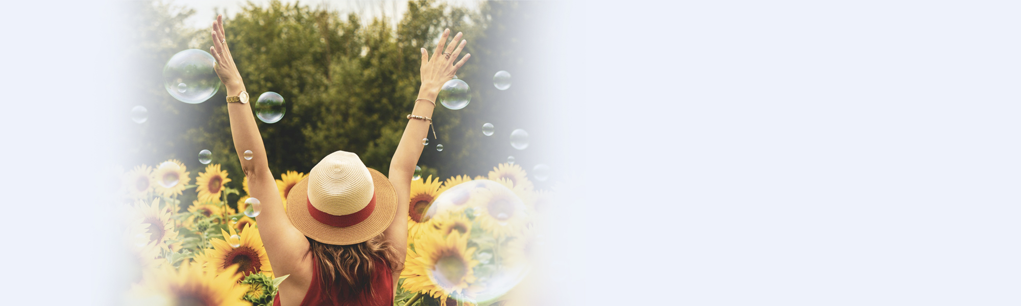 Foto einer Frau mit Sonnenhut in einem Sonnenblumenfeld, die Arme in die Luft gestreckt, umgeben von schwebenden Seifenblasen